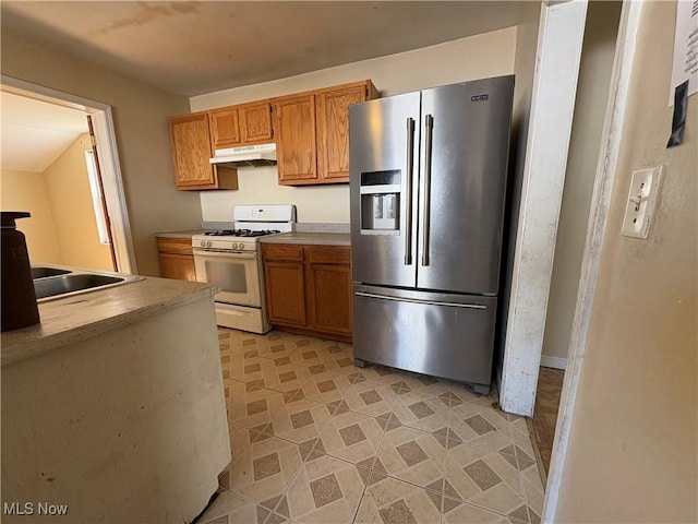 kitchen with brown cabinets, stainless steel fridge, under cabinet range hood, and white gas range