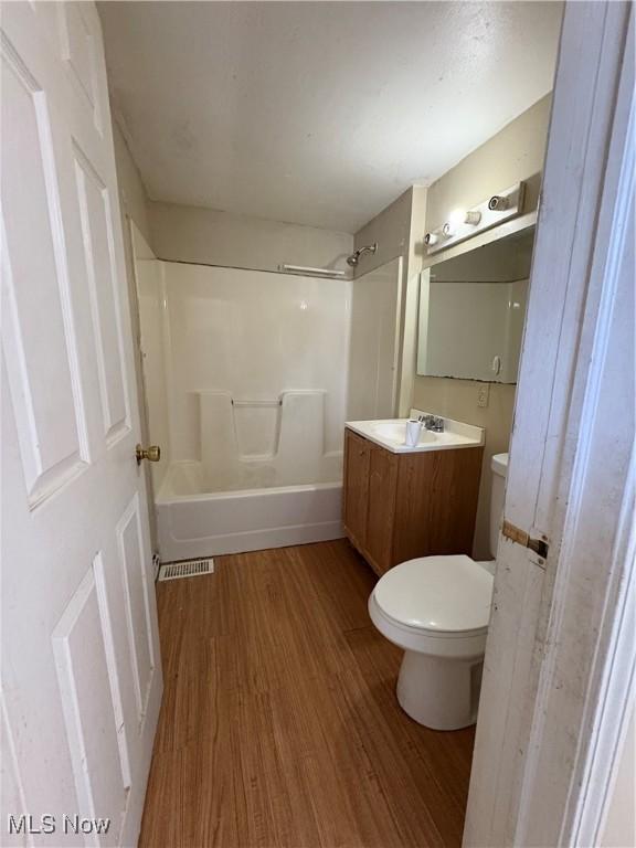 bathroom featuring visible vents, toilet, vanity, wood finished floors, and shower / bathtub combination