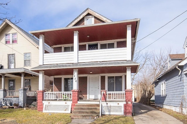 multi unit property featuring covered porch, roof with shingles, brick siding, and a balcony