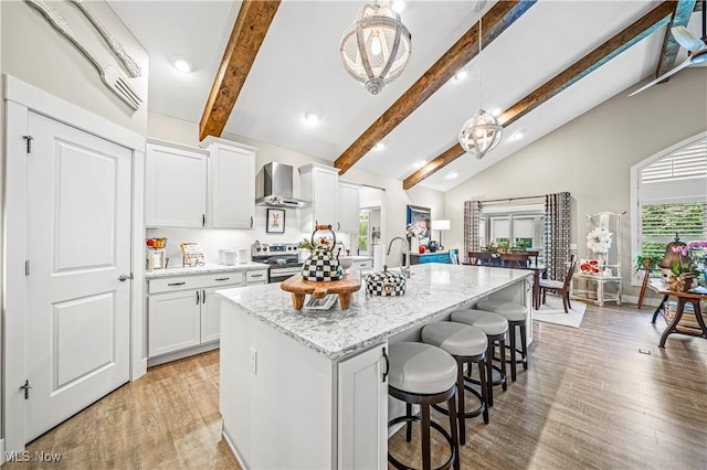 kitchen with a center island with sink, stainless steel electric range oven, wall chimney exhaust hood, light wood-style flooring, and a kitchen bar