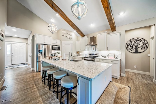 kitchen with wall chimney exhaust hood, a breakfast bar area, wood finished floors, stainless steel appliances, and a sink