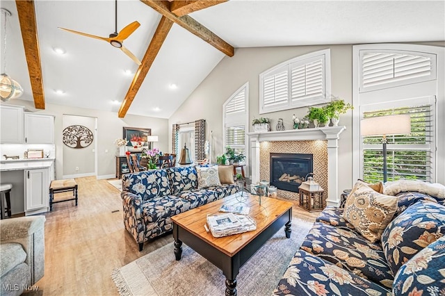 living room featuring light wood-type flooring, a wealth of natural light, beam ceiling, and a tiled fireplace