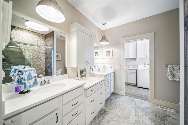 bathroom featuring washer / clothes dryer, a stall shower, two vanities, and a sink