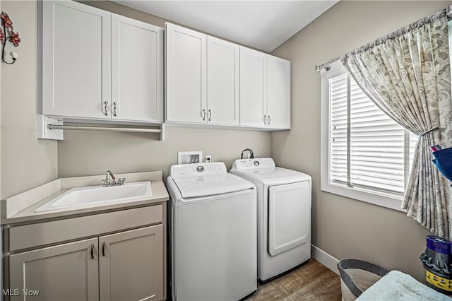 washroom with washing machine and clothes dryer, cabinet space, a sink, wood finished floors, and baseboards