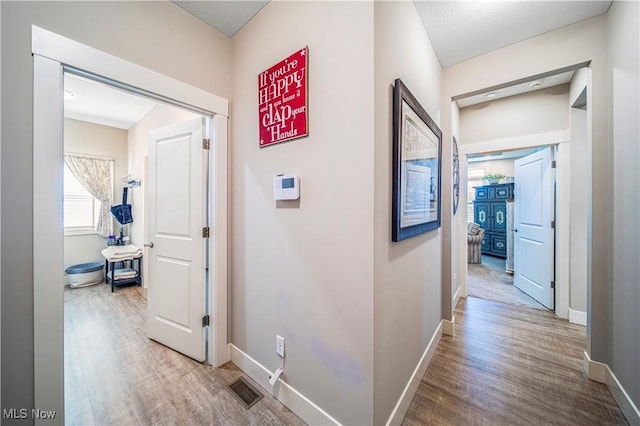 corridor with baseboards, visible vents, and wood finished floors