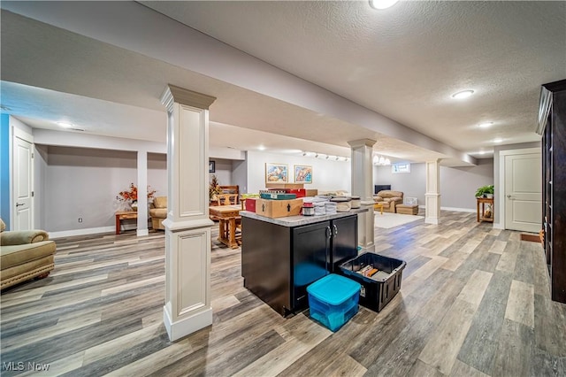 bar with light wood-type flooring, decorative columns, and a textured ceiling