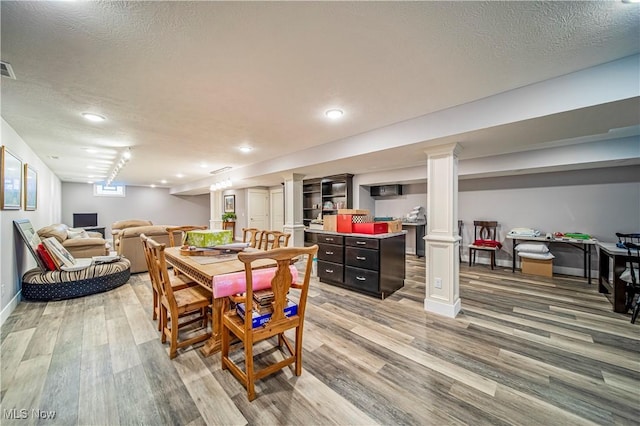 dining area with light wood finished floors, baseboards, a textured ceiling, and ornate columns