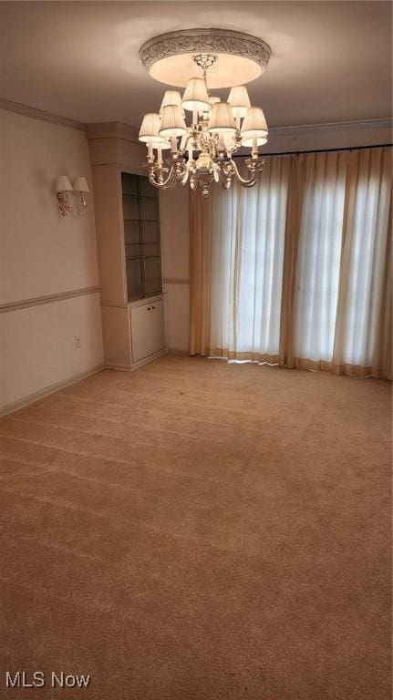 empty room featuring a chandelier, light colored carpet, crown molding, and baseboards