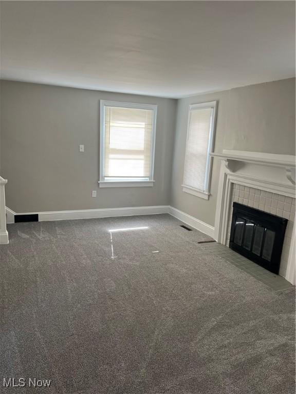 unfurnished living room with carpet, a tile fireplace, visible vents, and baseboards