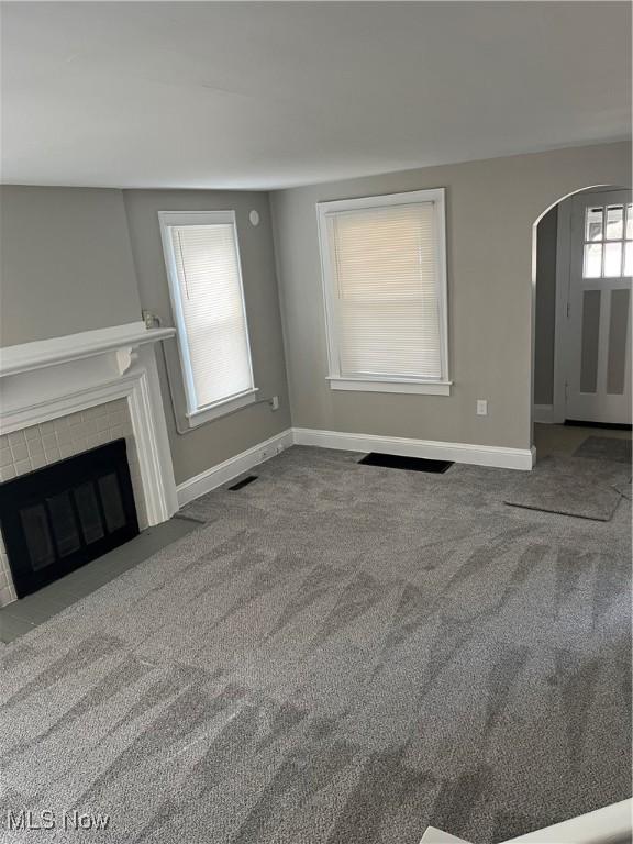 unfurnished living room with a fireplace with flush hearth, arched walkways, visible vents, and carpet