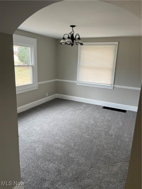 carpeted empty room featuring a chandelier, arched walkways, and baseboards