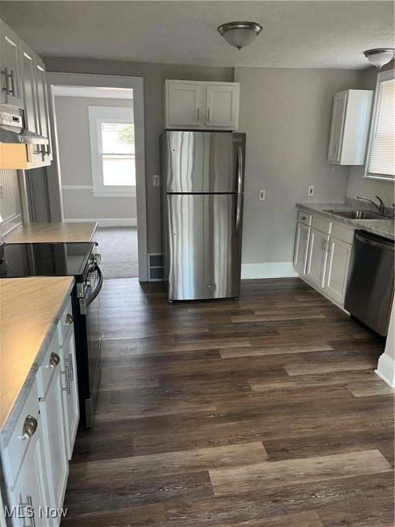 kitchen with baseboards, dark wood finished floors, appliances with stainless steel finishes, wall chimney range hood, and a sink