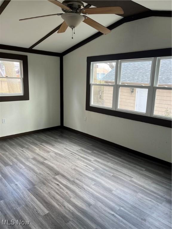 empty room featuring ceiling fan, vaulted ceiling, baseboards, and wood finished floors