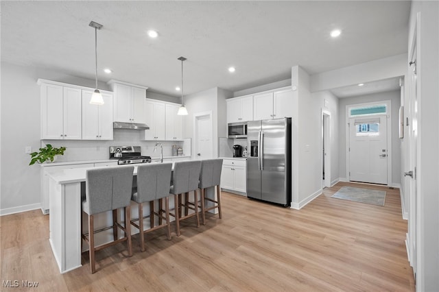 kitchen with a breakfast bar area, light wood-style flooring, under cabinet range hood, light countertops, and appliances with stainless steel finishes