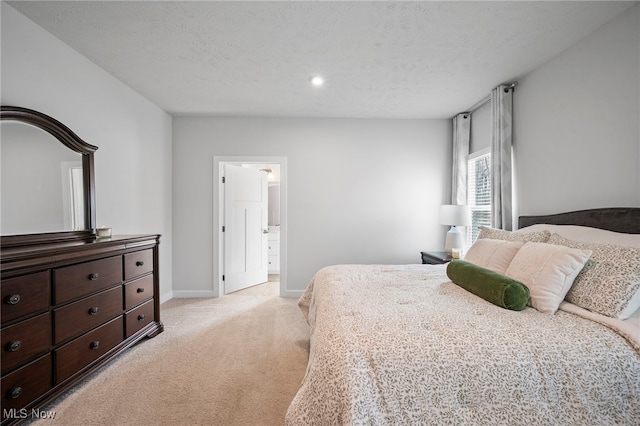 bedroom with a textured ceiling, baseboards, ensuite bathroom, and light colored carpet