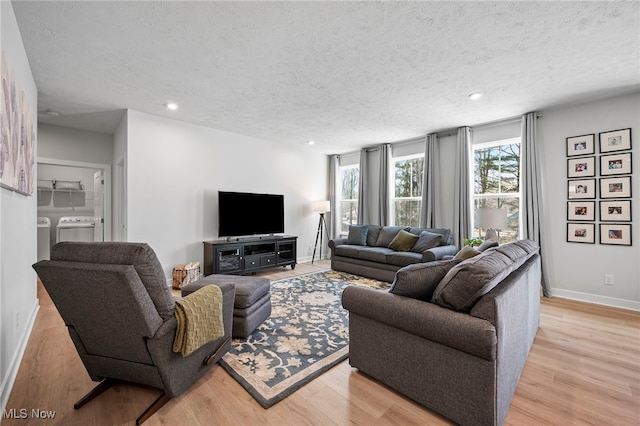 living room featuring a textured ceiling, light wood-type flooring, baseboards, and washer and dryer