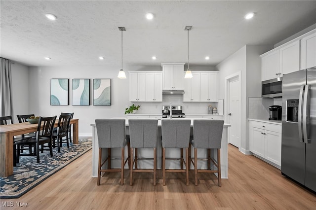 kitchen featuring stainless steel appliances, light wood-style flooring, white cabinets, a kitchen island with sink, and under cabinet range hood