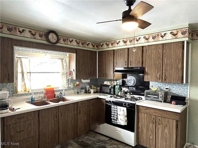 kitchen featuring gas range oven, light countertops, a sink, black microwave, and under cabinet range hood