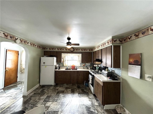 kitchen with arched walkways, range with gas stovetop, freestanding refrigerator, light countertops, and a sink