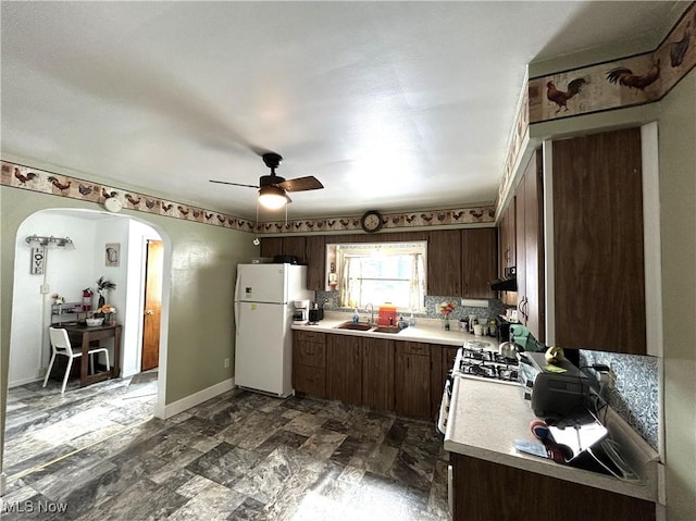 kitchen featuring arched walkways, light countertops, backsplash, a sink, and white appliances