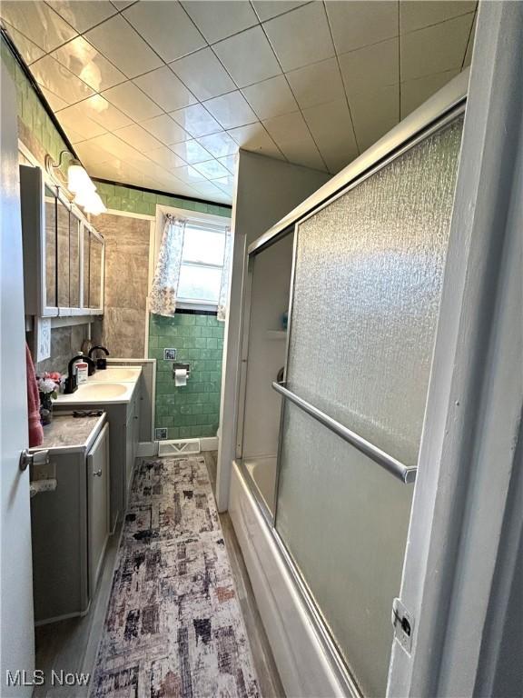 full bathroom with tile walls, vanity, and bath / shower combo with glass door