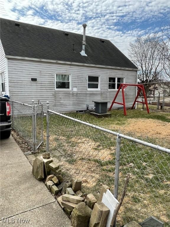 rear view of property with fence, central AC, and roof with shingles