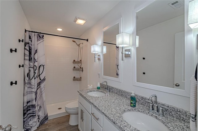 bathroom with toilet, tiled shower, a sink, and visible vents