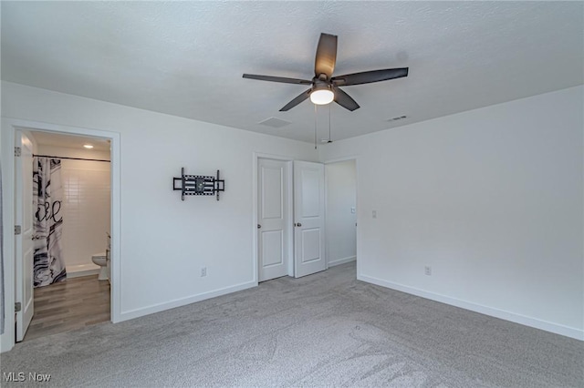 unfurnished bedroom featuring a textured ceiling, connected bathroom, visible vents, baseboards, and carpet