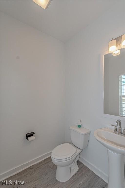 half bathroom with toilet, a sink, baseboards, and wood finished floors