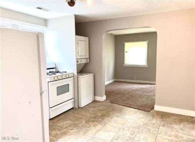 kitchen with white appliances, baseboards, visible vents, and stacked washer and clothes dryer