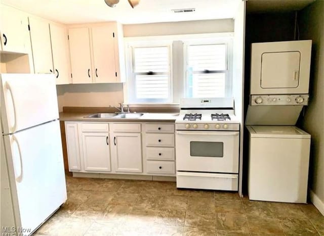 kitchen with light countertops, visible vents, stacked washer / dryer, a sink, and white appliances