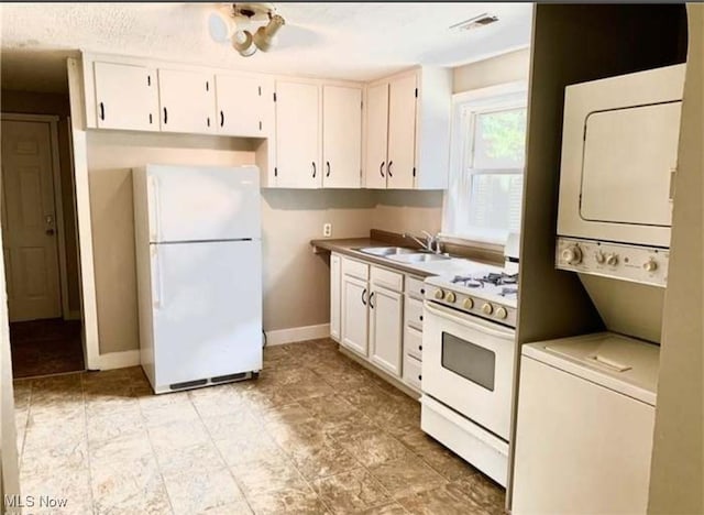 kitchen with white appliances, stacked washing maching and dryer, white cabinetry, and a sink