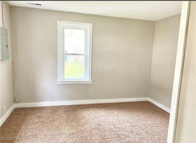 carpeted spare room featuring visible vents, electric panel, and baseboards