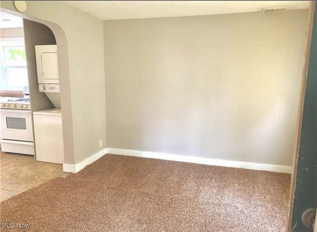 carpeted spare room with visible vents, baseboards, arched walkways, and stacked washer / drying machine