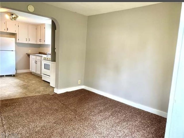 kitchen featuring arched walkways, carpet, white cabinetry, white appliances, and baseboards