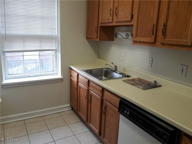 kitchen featuring brown cabinetry, white dishwasher, light countertops, a sink, and light tile patterned flooring