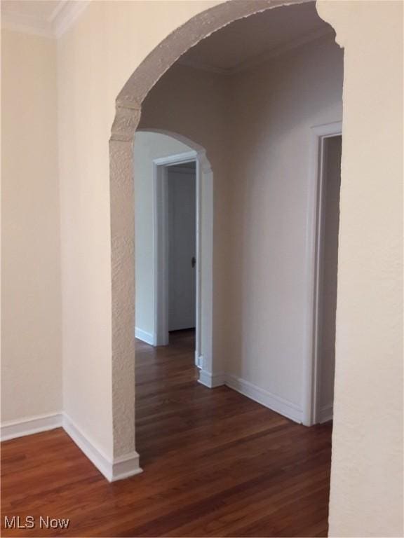 corridor with arched walkways, dark wood finished floors, and baseboards