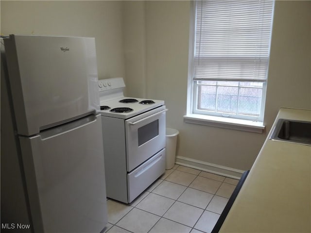 kitchen with light tile patterned floors, a sink, baseboards, white range with electric stovetop, and freestanding refrigerator