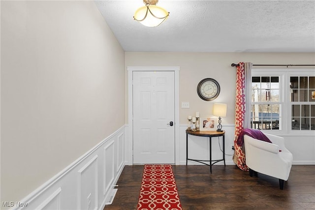 foyer featuring a textured ceiling, wainscoting, wood finished floors, and a decorative wall