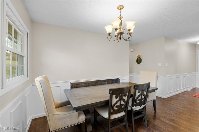 dining space featuring a notable chandelier, a textured ceiling, dark wood-type flooring, and wainscoting