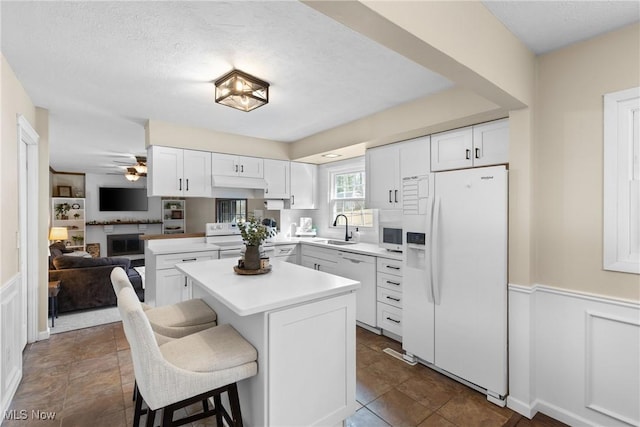 kitchen featuring a wainscoted wall, white appliances, a sink, white cabinets, and light countertops