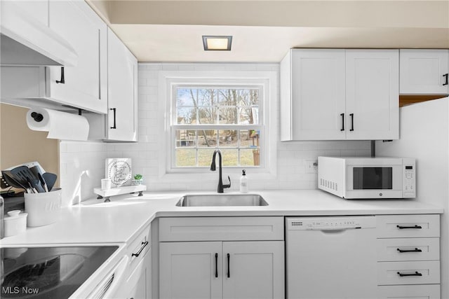 kitchen with under cabinet range hood, white appliances, a sink, light countertops, and decorative backsplash