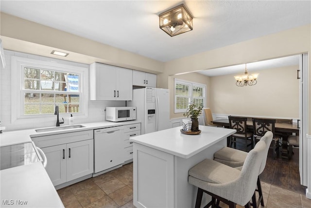 kitchen with backsplash, a kitchen island, a sink, white appliances, and a kitchen bar