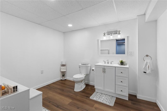 bathroom with a drop ceiling, wood finished floors, toilet, and baseboards