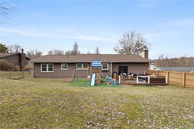 back of property with a playground, a fenced backyard, a lawn, a wooden deck, and a chimney