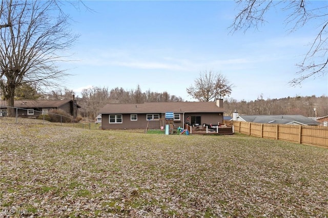 rear view of property featuring a chimney, a fenced backyard, a lawn, and a deck