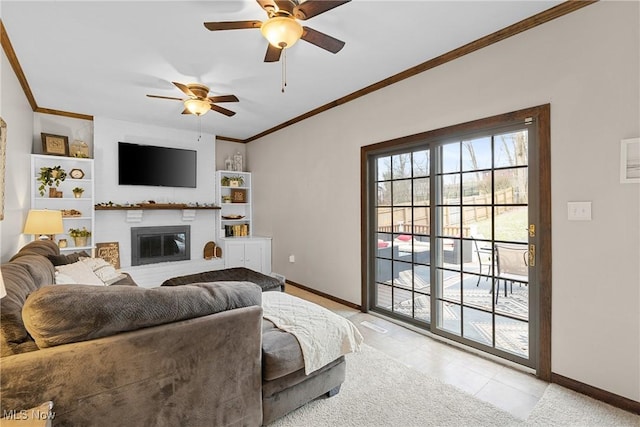 living room with built in shelves, a ceiling fan, baseboards, a brick fireplace, and crown molding