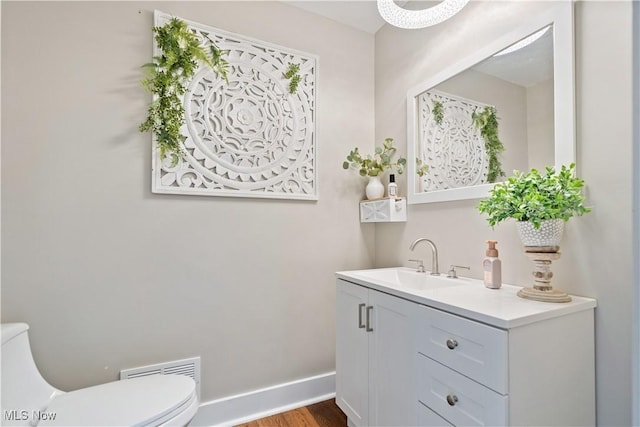 bathroom featuring visible vents, toilet, vanity, wood finished floors, and baseboards