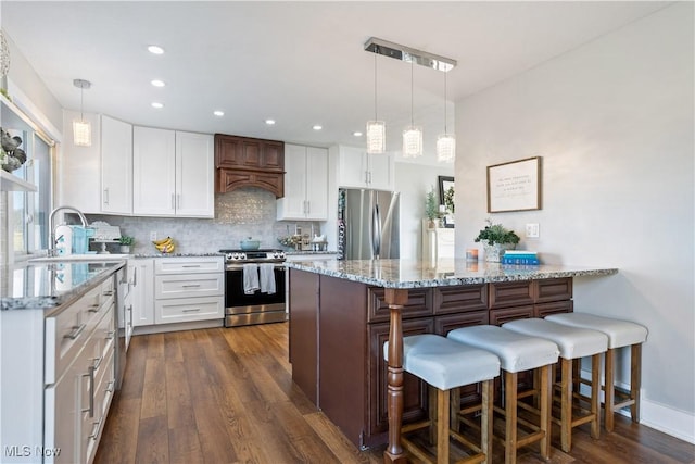 kitchen with stainless steel appliances, dark wood-type flooring, white cabinets, a kitchen breakfast bar, and tasteful backsplash