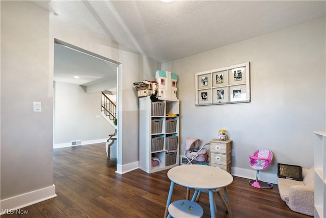 recreation room featuring wood-type flooring, visible vents, baseboards, and a textured ceiling